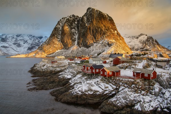 Fishermen's Village in front of snowy mountain range at the coastline in winter, Lofoten, Norway,