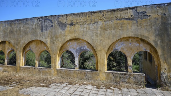 Dilapidated yellow arches in the exterior of a ruined building with visible structural damage, Lost
