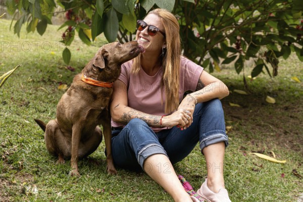 Woman in her 40s wearing sunglasses with a joyful expression receives a lick from her pet while