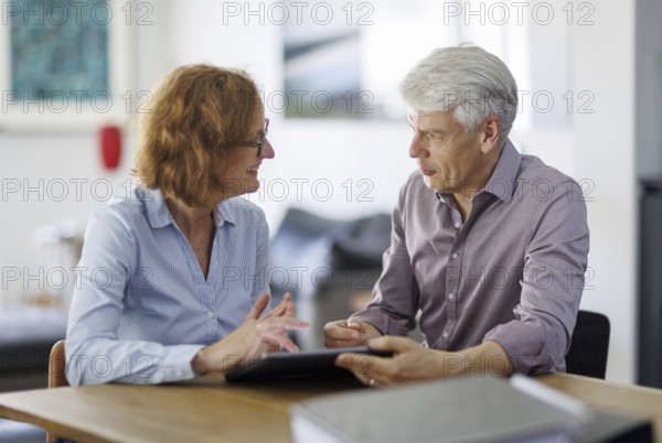 Symbolic photo. A woman and a man sit together at a table with a tablet and talk. Berlin, 13.08