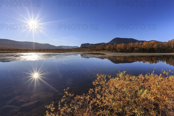 Mountains reflected in lake, autumn colours, sun, sun star, bright, friendly, Nikkaluokta, Laponia,