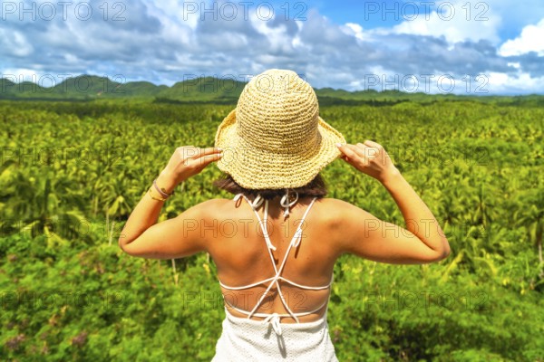 Young woman enjoying the view of a wide coconut plantation in siargao island, philippines, holding