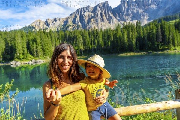 Mother and son smiling and enjoying summer holidays at lake carezza with the latemar mountain range