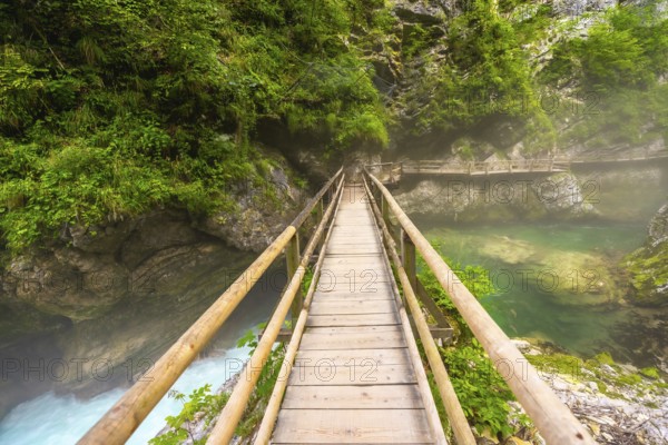 Scenic view of a wooden footbridge spanning a crystal clear emerald river flowing through the