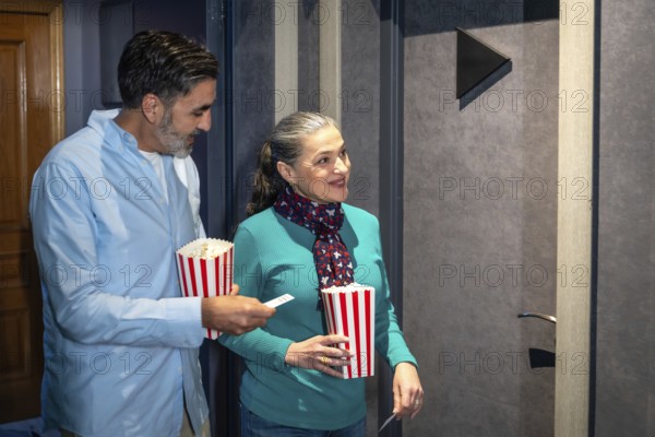 Happy mature couple entering cinema theater with popcorn and tickets, enjoying a night out together