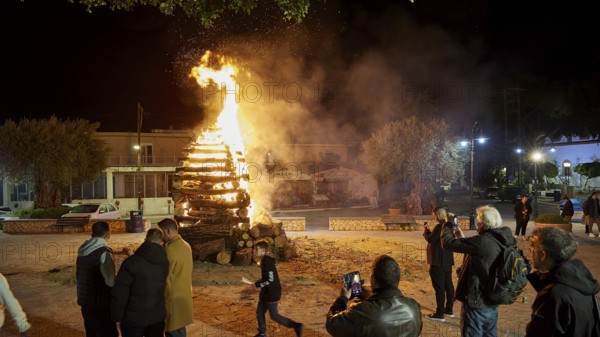 People gather around a burning pile of wood at night, some take photos, Easter fire Psinthos, Holy