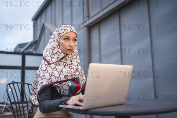 Arab girl with a white veil at the computer on the terrace of a coffe shop, contrabass with the