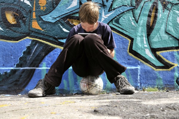 Ten-year-old boy playing with his Nintendo in front of a graffiti wall, football pitch, Germany,