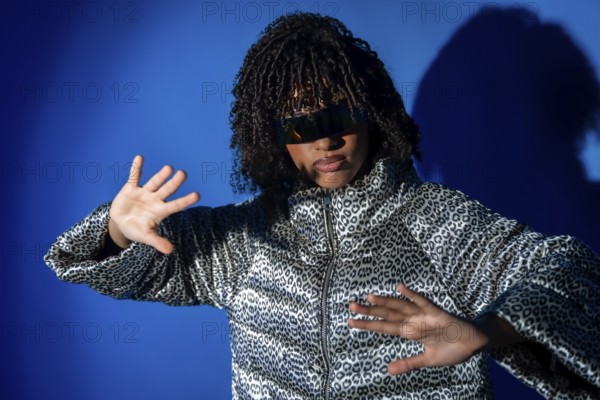 Young woman with curly hair and sunglasses dancing with hands up, wearing a patterned jacket on a
