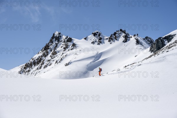 Ski tourer on the descent, minimalist winter landscape, white snow and dark mountains on the