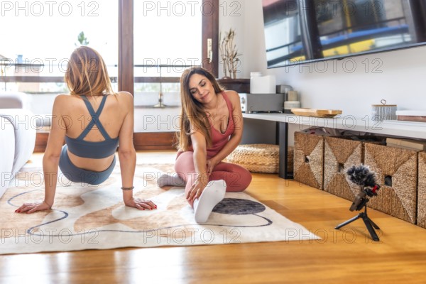 Two women wearing sportswear practicing and recording online yoga class at home in their living