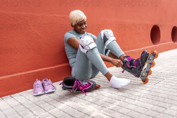 African woman with blonde short hair putting on inline skates sitting on ground in the street