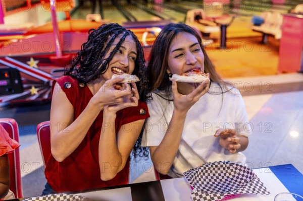 Two joyful young women sharing delicious pizza while enjoying a fun filled day at the bowling