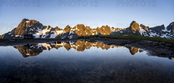 Rocky mountain peaks reflected in a small pond, mountain landscape with alpenglow at sunrise, at