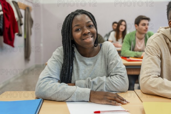 Young black female student is smiling while sitting at her desk in a classroom during a lesson with