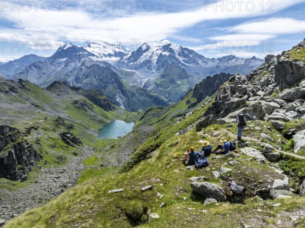 Hikers taking a break, mountain lake Lac de Louvie with glaciated summit of the Grand Combin, Val