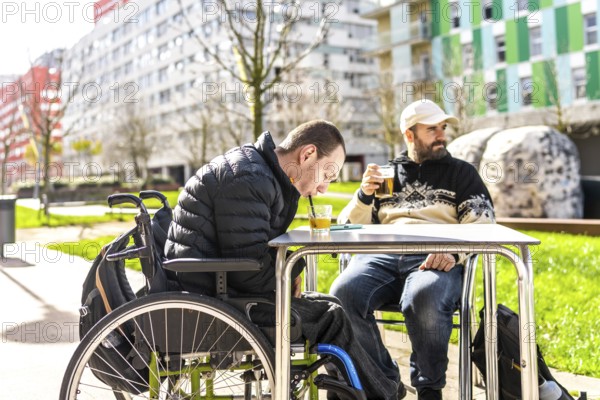 Two men enjoy drinks at an outdoor cafe, one using a wheelchair, demonstrating inclusivity and