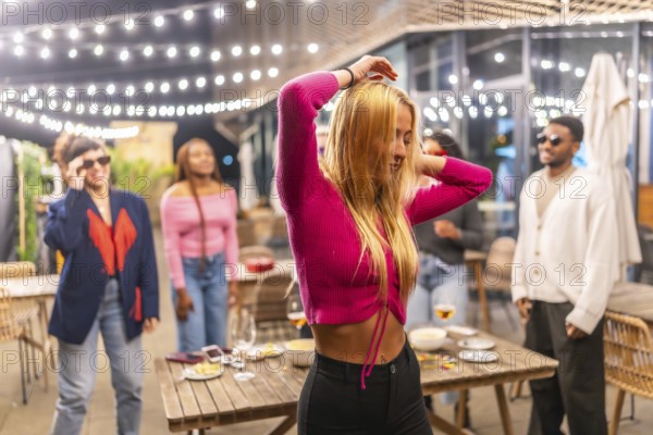 Blonde sensual woman dancing with friends at night party at the terrace of a bar decorated with