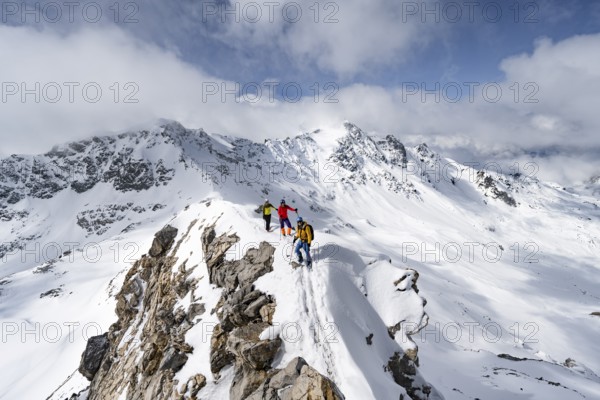 Three mountaineers climbing the narrow ridge of Piz Laviner, view of mountain panorama in winter