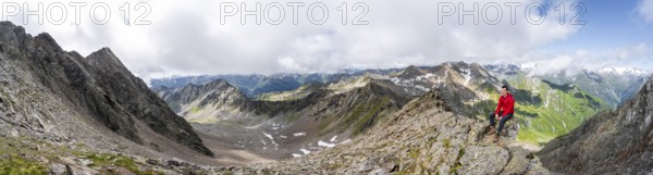 Panorama, mountaineer sitting on a rock, on a steep rocky ridge, on the summit of the Lasörling,