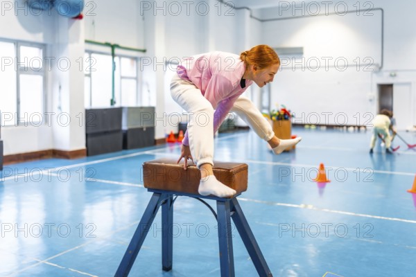 Girl practicing gymnastics, balancing on pommel horse in school gym, showing determination and