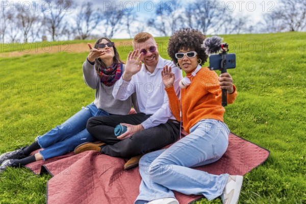 Three content creators waving and filming video with smartphone and external microphone in a park