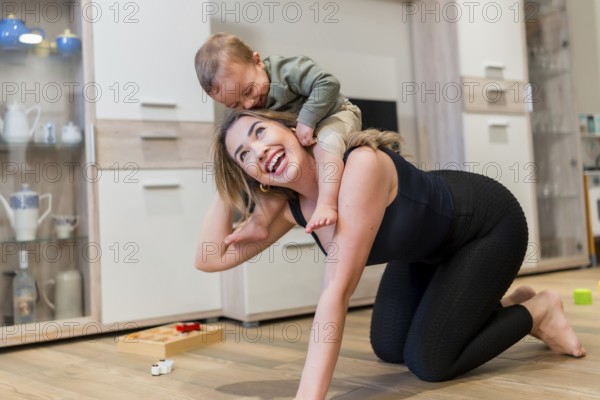 Young mother joyfully playing with her baby son, carrying him on her back while enjoying quality