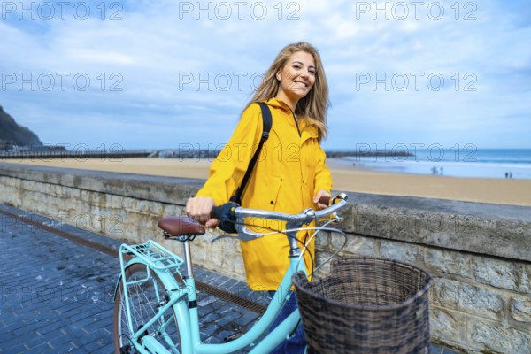 Happy young woman walking with her bicycle on the boardwalk by the beach, enjoying the fresh air