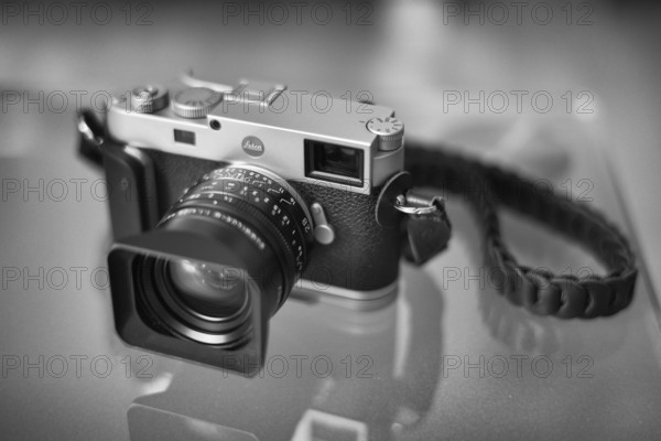 Leica M11 with Kamerakraft Grip and RocknRoll carrying strap standing on glass table, black and