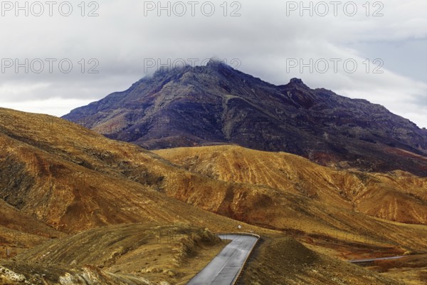 A winding road leads through a mountainous landscape under a cloudy sky, Pajara, Fuerteventura,