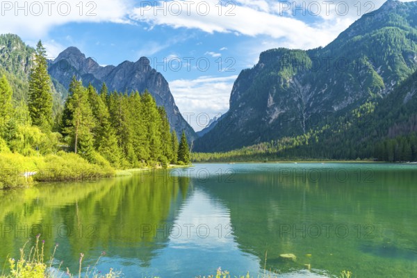 Stunning alpine landscape reflecting on lake dobbiaco's emerald waters, surrounded by lush