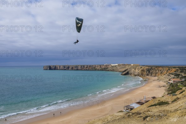 Sagres, Algarve, Portugal - Paraglider flying on the town beach Praia da Mareta, behind the sea