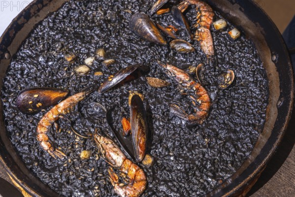 Close up of black paella with shrimps, mussels and other seafood, cooked and ready to be served in