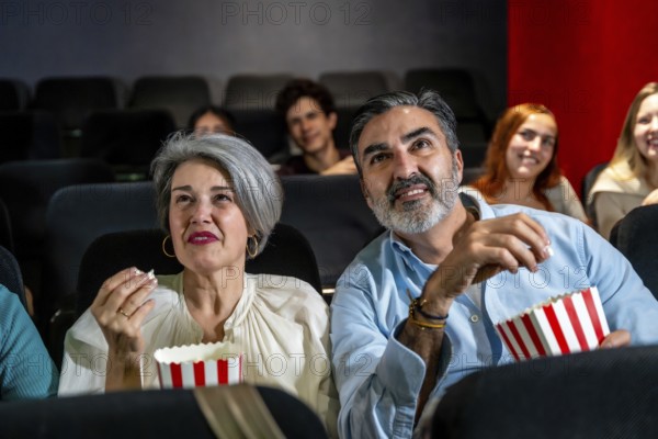 Senior couple watching a movie and eating popcorn, enjoying a night out at the cinema with other