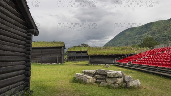 Traditional wooden houses with grass sod roofs, rows of seats with red plastic chairs, ready for an