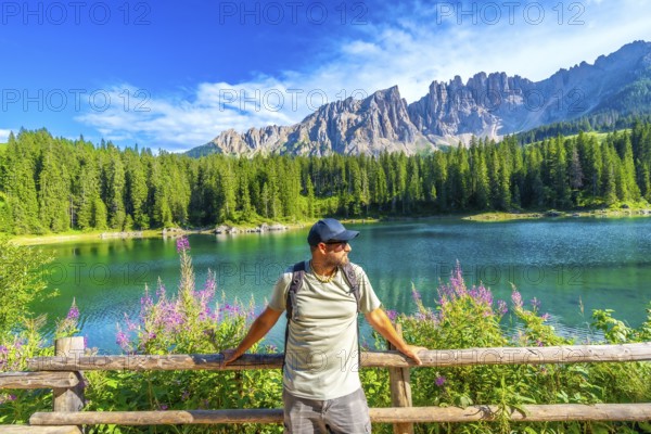 Hiker relaxing by a wooden fence, admiring the stunning turquoise waters of lake carezza with the