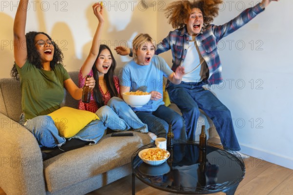 Group of young multi ethnic people enjoying a sports event on television, drinking beer and eating