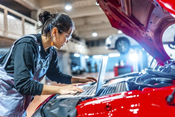 Young female mechanic using a laptop while inspecting a car engine in a professional auto repair