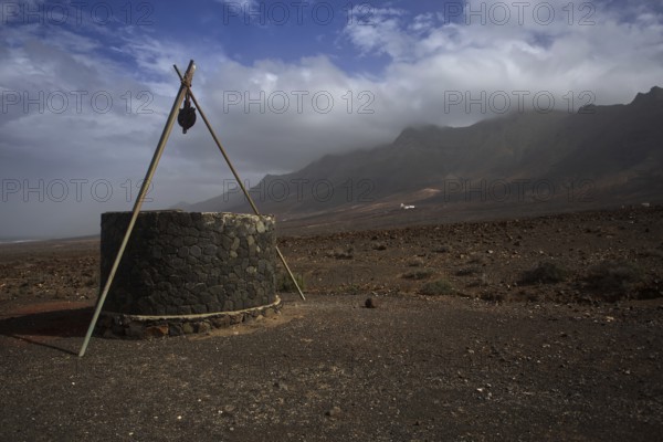 Stone fountain in lonely, barren volcanic landscape near Cofete in front of cloudy mountains,