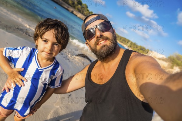 A man and a boy are posing for a picture on a beach. The boy is wearing a blue and white striped