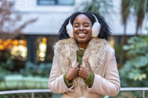 Happy young woman wearing cozy earmuffs and a stylish winter coat, smiling brightly while enjoying