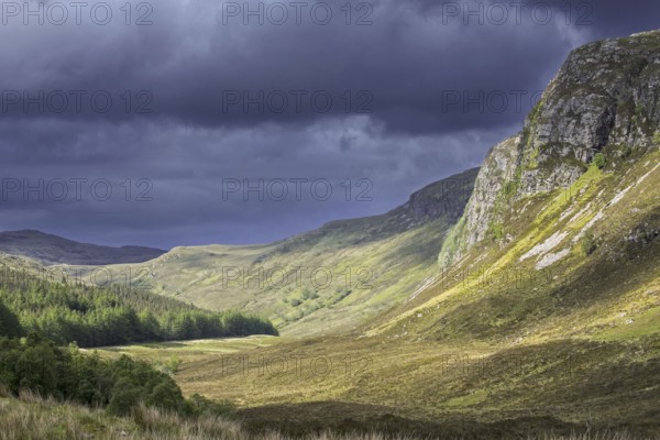 Mountain scenery showing dark rain clouds rolling in over sunny hillside and valley in Wester Ross,