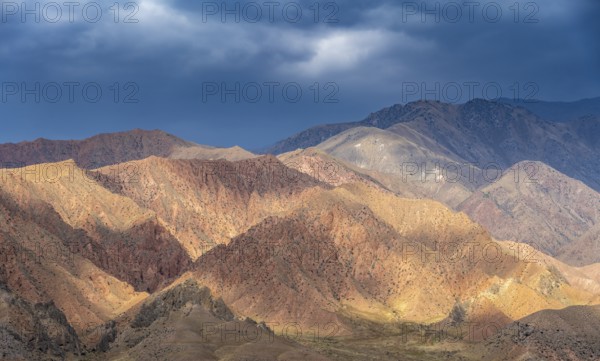 Red and orange mountains in atmospheric light, dramatic cloudy sky, mountain landscape near
