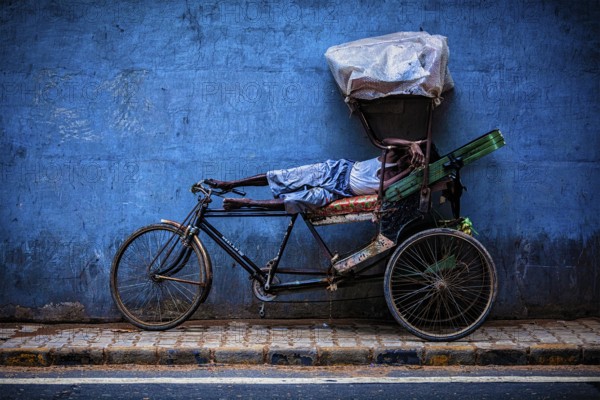 DELHI, INDIA, SEPTEMBER 11, 2011: Indian cycle rickshaw driver sleeping on his bicycle in the
