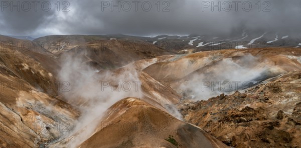 Steaming streams between colourful rhyolite mountains with snowfields, Hveradalir geothermal area,