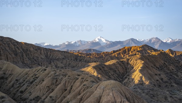 Landscape of eroded hills at sunrise, badlands, white mountain peaks of the Tian Shan Mountains in
