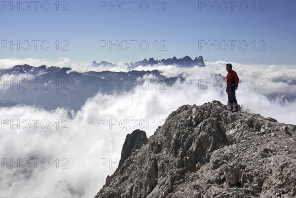 Mountaineer looking from the Cima Scalieret over blanket of clouds and mountain peaks of the
