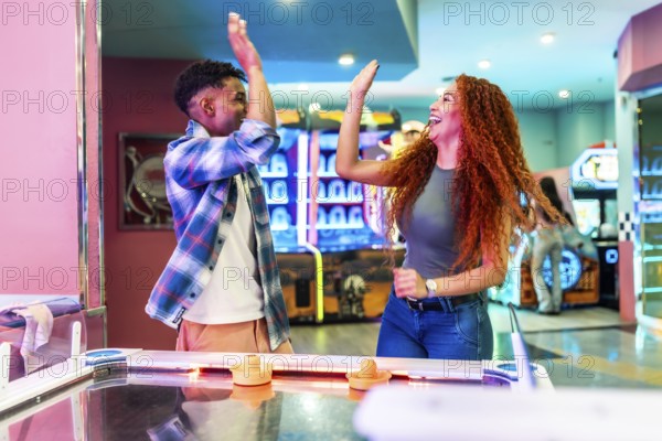 Two friends giving high five while enjoying a game of air hockey in a vibrant entertainment center,