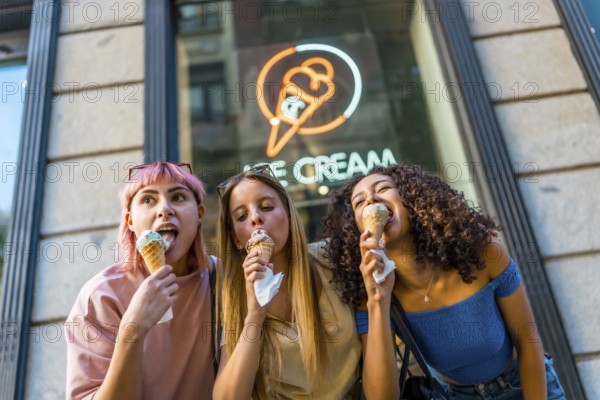 Low angle view photo of three diverse female friends enjoying eating a delicious ice cream outside