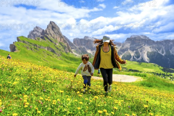 Mother and son running through a field of wildflowers in the italian dolomites mountains, enjoying